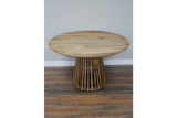 Round wooden dining table with slatted base, natural finish, front view on wooden floor against gray wall.