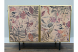 Small cabinet with two doors, black metal legs, gold frame, and leaf-patterned front panels in earthy tones.