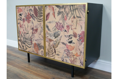 Small black metal cabinet with gold-framed doors featuring pink and purple pressed leaf and fern print, angled view.