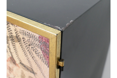 Small black metal cabinet with gold leaf detailed door, corner view showing hinge and paint chipping on edge.