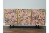 Large wooden cabinet with three leaf-patterned doors in muted pink, brown, and gold, standing on black legs.