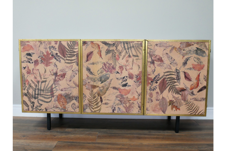 Large wooden cabinet with three leaf-patterned doors in muted pink, brown, and gold, standing on black legs.