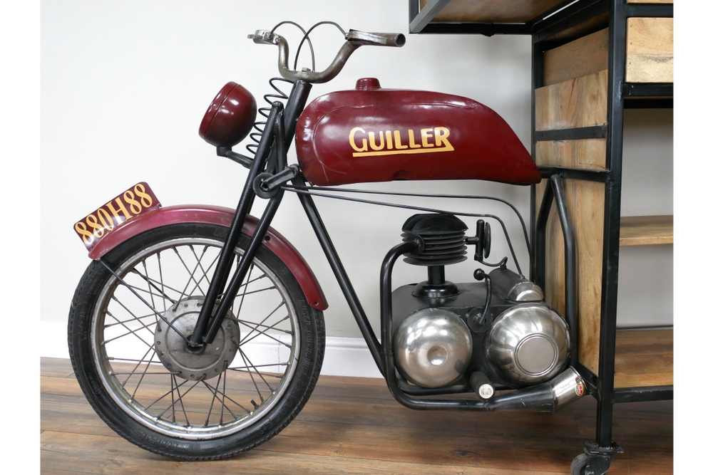 Metal and wood motorbike-shaped bar cabinet in red and black, side view, indoors on wooden floor near shelving unit.