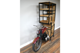 Industrial style motorbike bar cabinet with black metal frame and wooden shelves on hardwood floor, angled view.