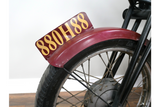 Close-up angle of motorbike bar cabinet wheel with black metal spokes, maroon fender, and yellow lettering plate.