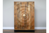 The Solstice Wine Cabinet features a natural wood finish with a striking circular carved design and a round gold knob, resting on a sleek black base