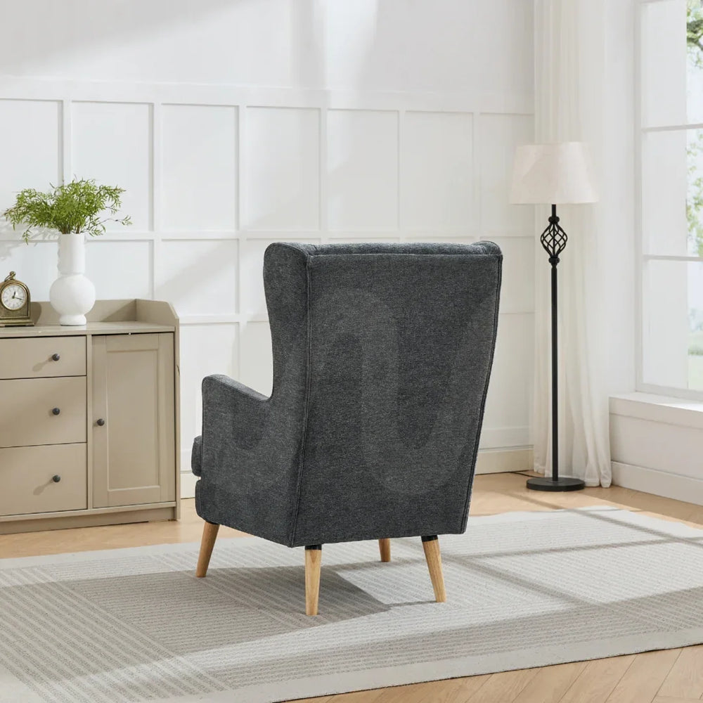 Dark grey wing chair with wooden legs in bright living room beside sideboard and floor lamp
