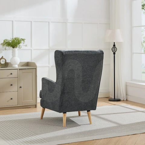 Dark grey wing chair with wooden legs in bright living room beside sideboard and floor lamp
