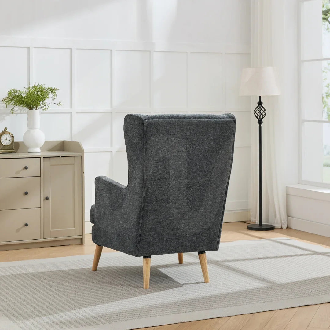 Dark grey wing chair with wooden legs in bright living room beside sideboard and floor lamp