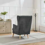 Dark grey wing chair with wooden legs in bright living room beside sideboard and floor lamp
