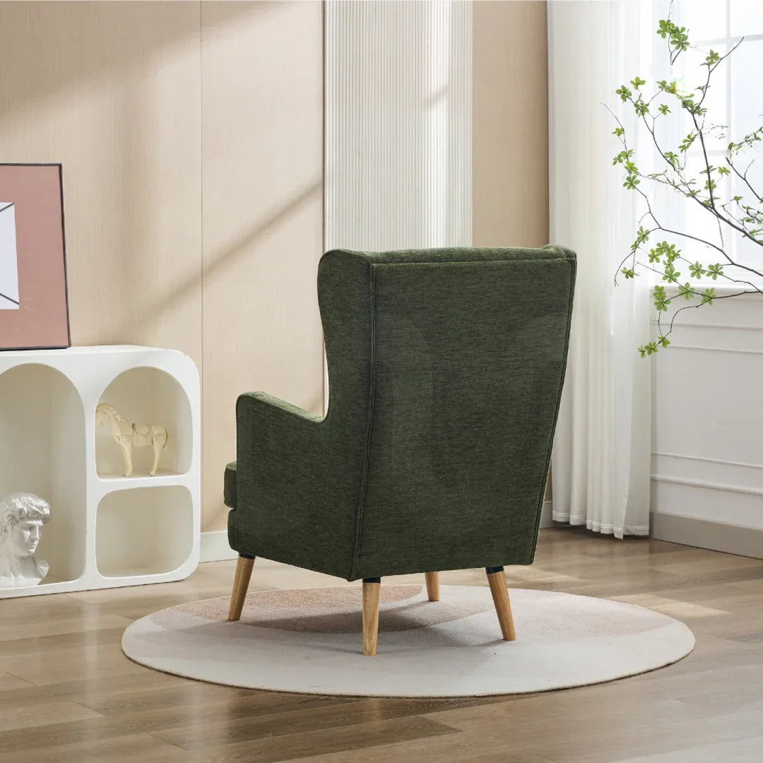 Moss green wing chair with pillow on wooden legs, shown from back in modern living room