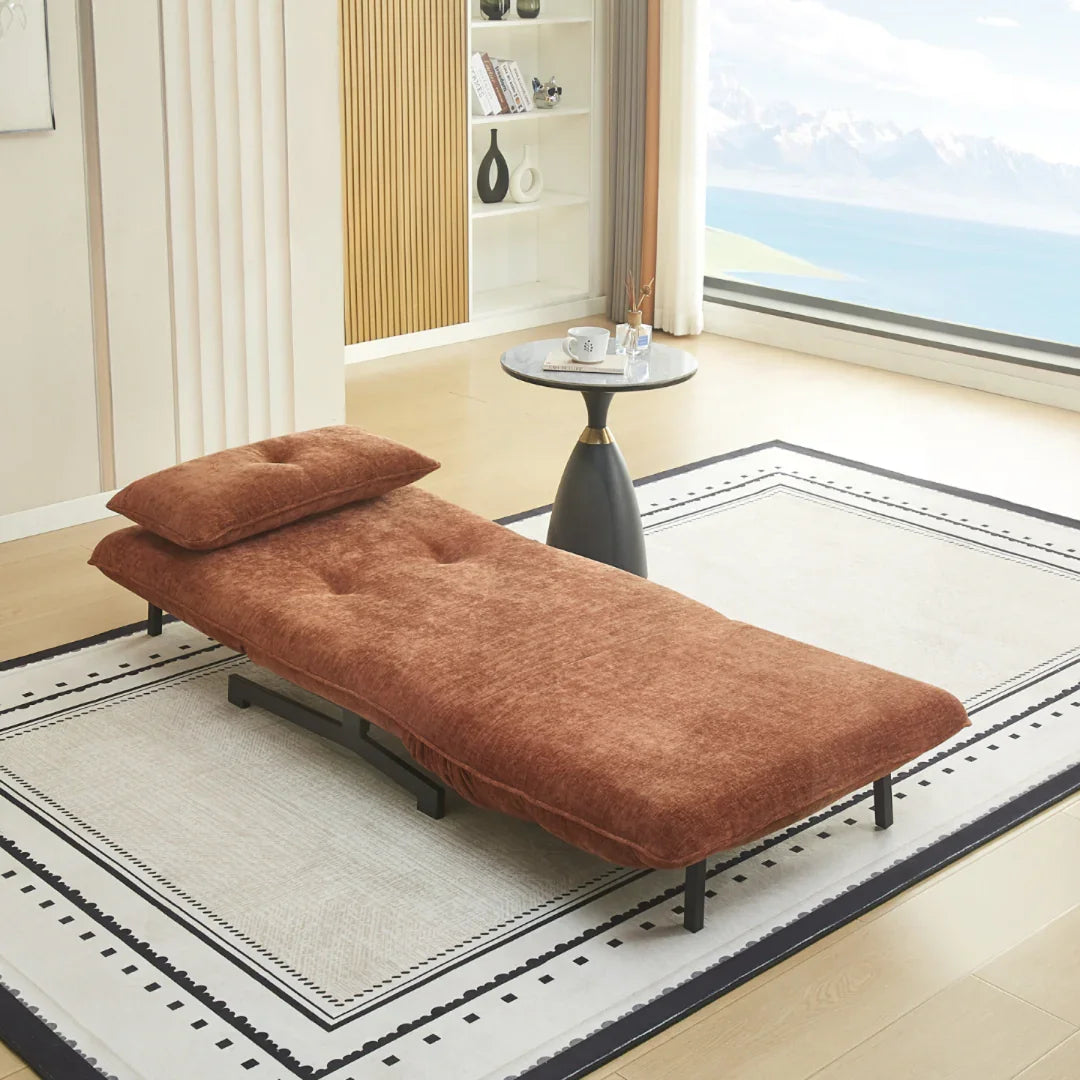 Single sofa bed in deep terra fabric with pillow, set on rug beside modern round side table