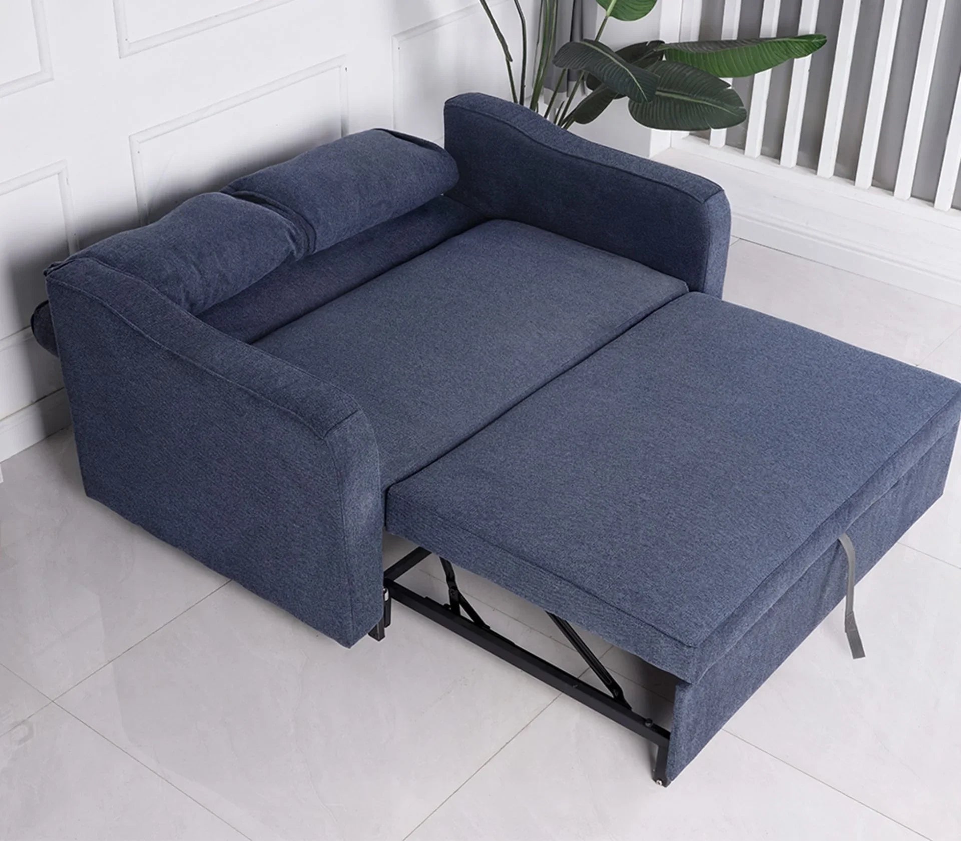 Denim blue sofa bed unfolded on tiled floor with metal frame and armrests