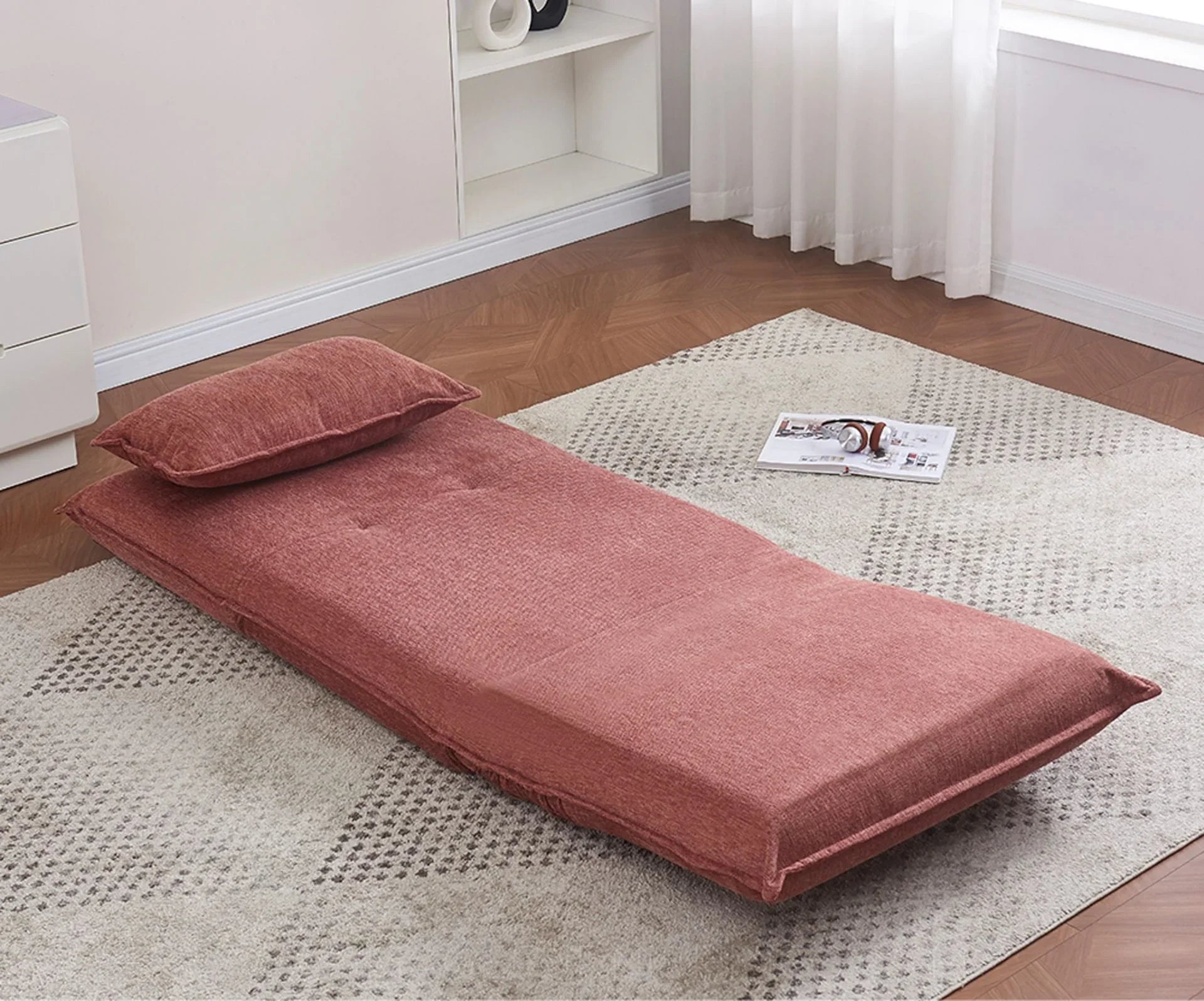 Rust fabric sofa bed with cushion shown flat on a patterned rug in a bright living room