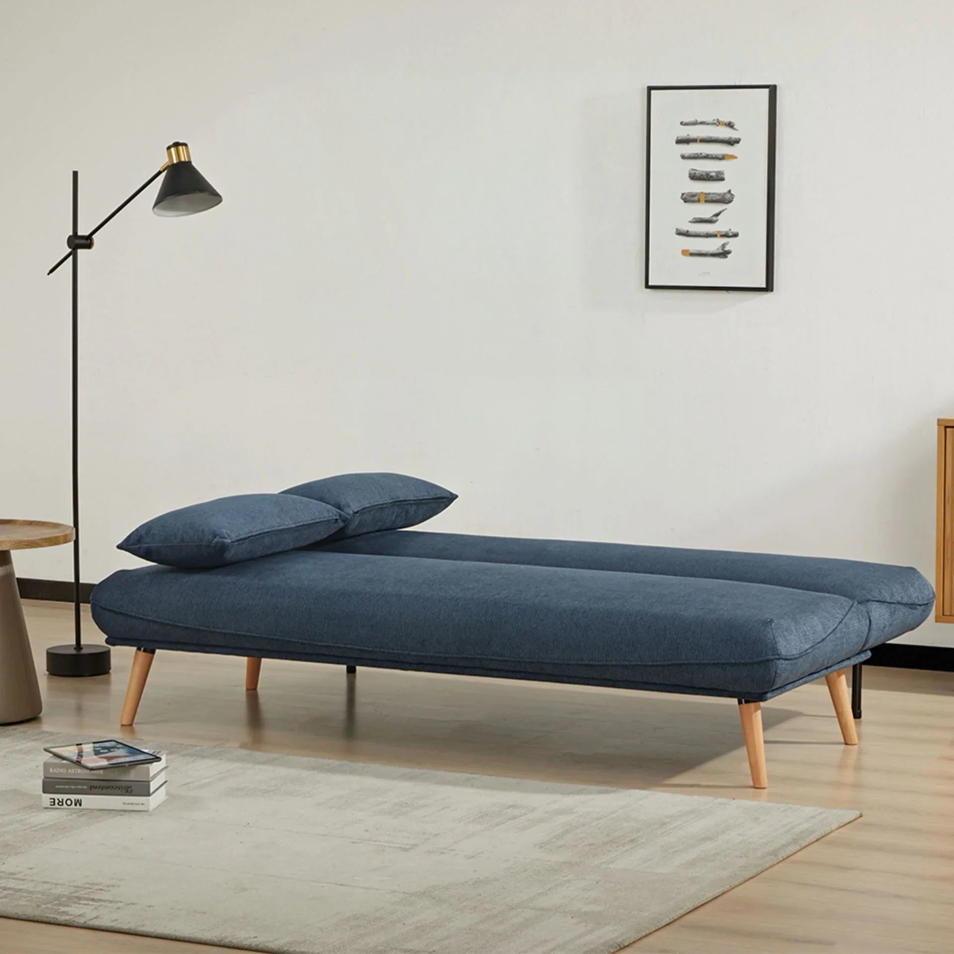 Blue fabric sofa bed with wooden legs styled in a modern living room setting