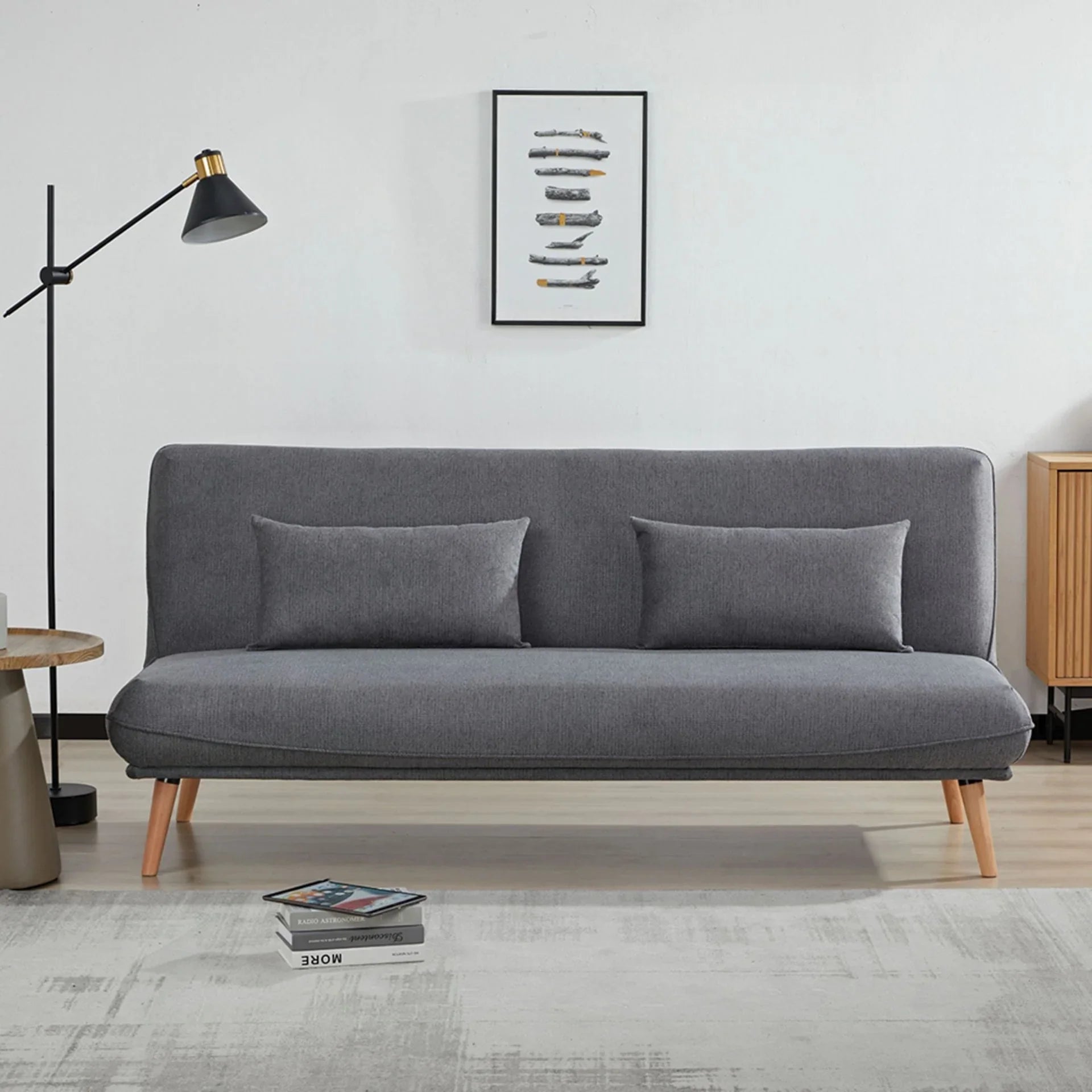 Dark grey sofa bed with wooden legs and two cushions in modern living room setting