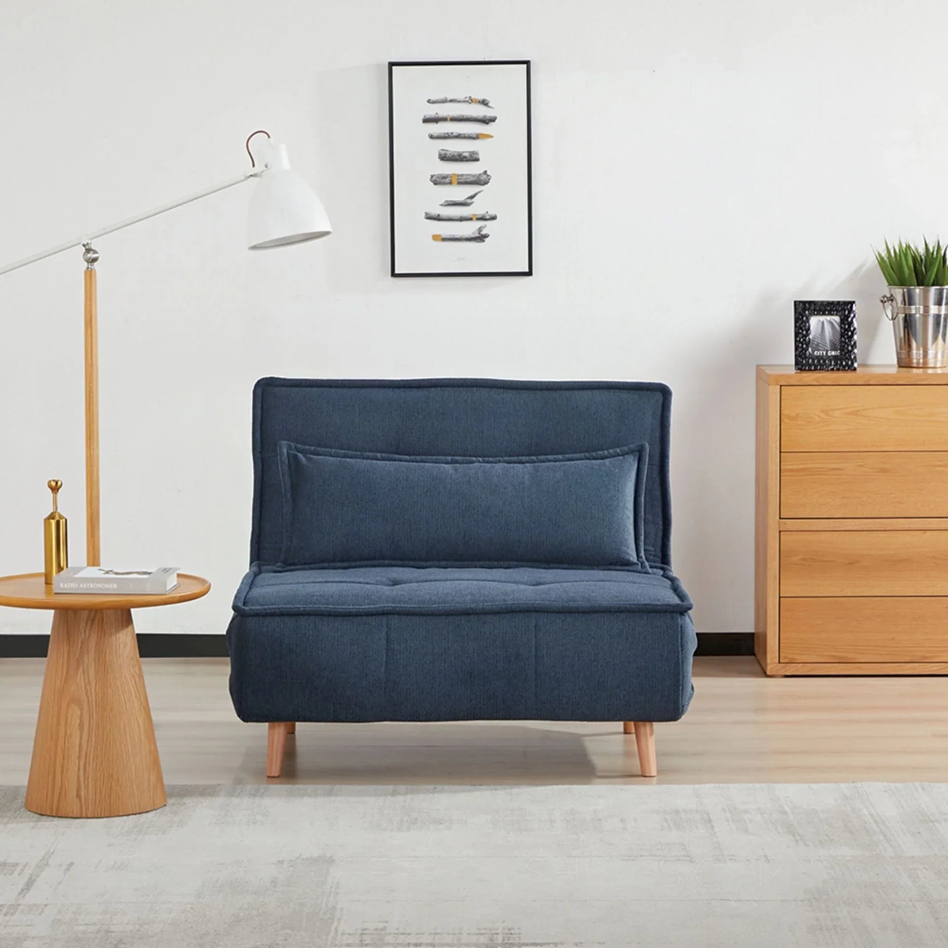 Blue fabric sofa bed with cushion, wooden legs, beside dresser in modern living room