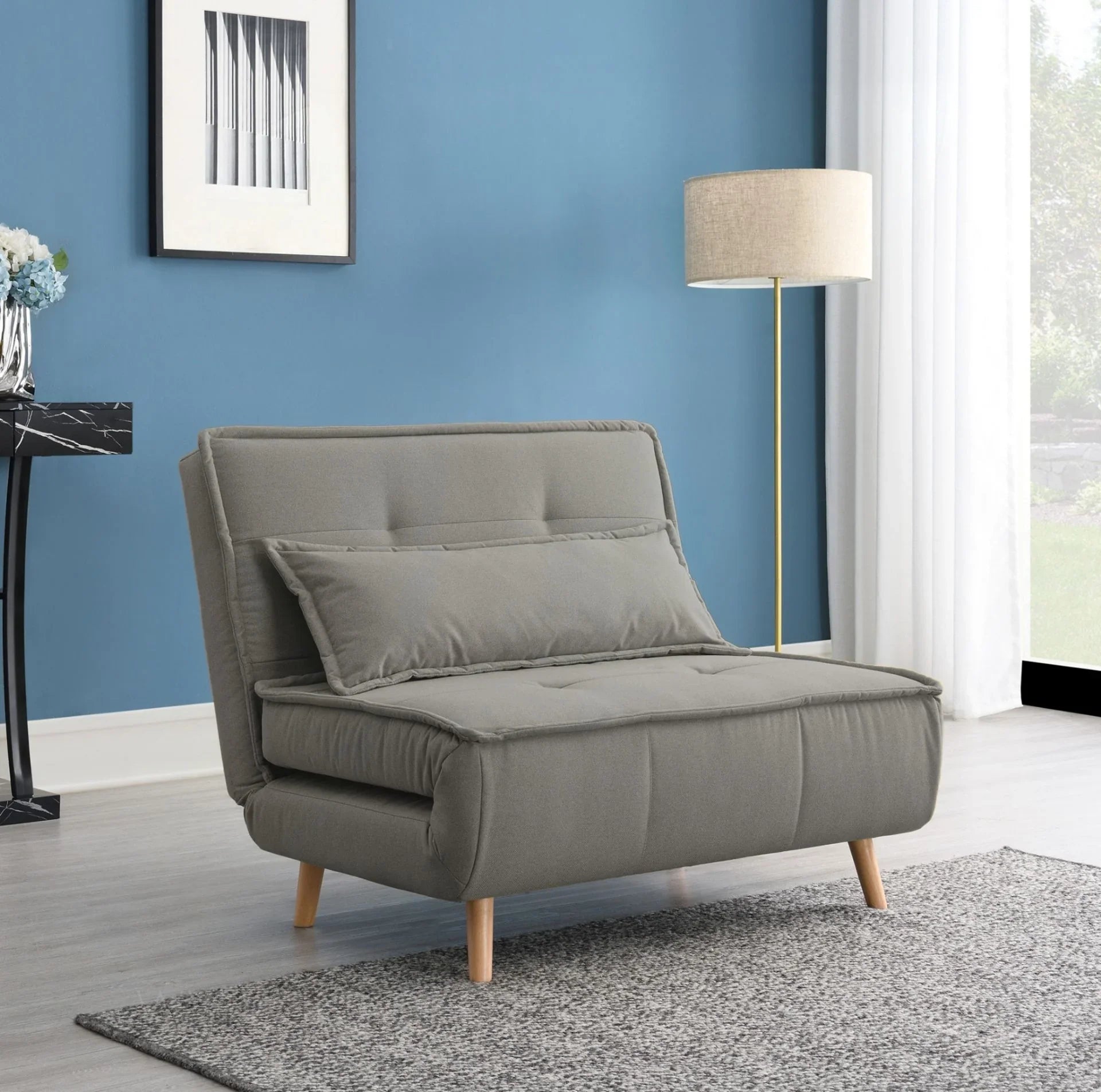 Dark grey sofa bed with cushion, wooden legs, in modern living room with blue wall