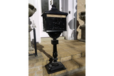 Black cast iron post box with gold lettering on pedestal by front door steps