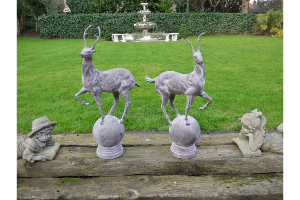 Pair of decorative deer garden statues on stone orbs with lawn and fountain backdrop