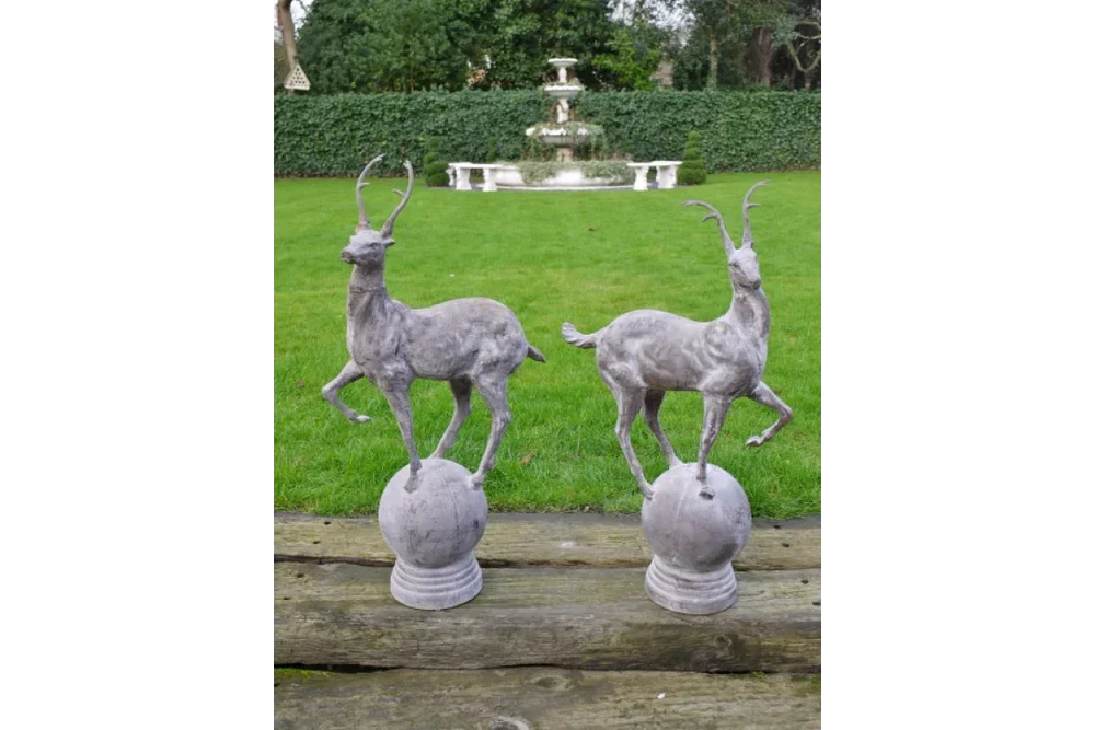 Pair of grey deer garden ornaments on plinths with grass lawn and fountain backdrop