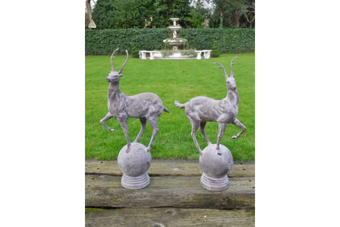 Pair of grey deer garden ornaments on plinths with grass lawn and fountain backdrop