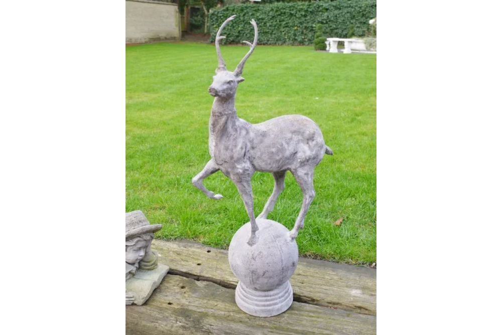 stone deer garden ornament with antlers standing on sphere on wooden decking