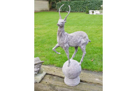 stone deer garden ornament with antlers standing on sphere on wooden decking