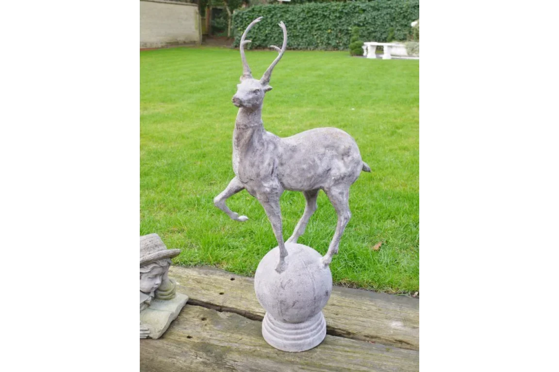 stone deer garden ornament with antlers standing on sphere on wooden decking
