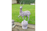 stone deer garden ornament with antlers standing on sphere on wooden decking