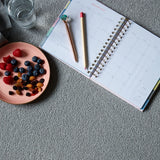 A cozy setup featuring a January 2020 planner with a pen and pencil, accompanied by a plate of fresh berries, nuts, and a glass of water on a soft carpet.