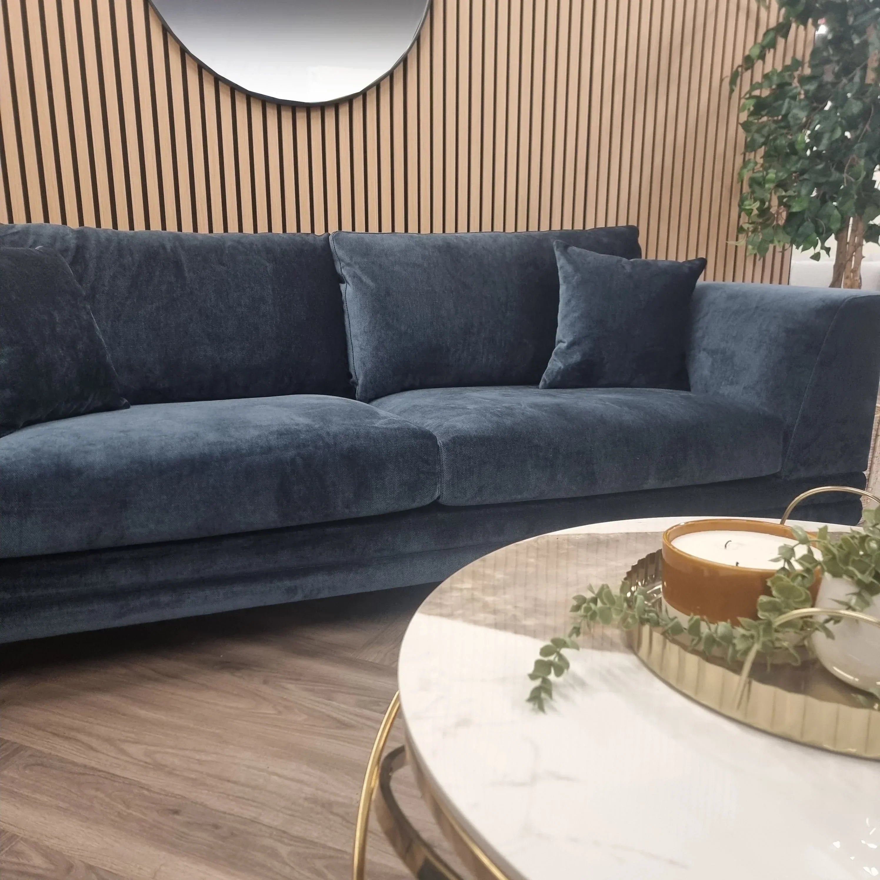Dark blue velvet sofa with plush cushions in front of wood panel wall and round coffee table