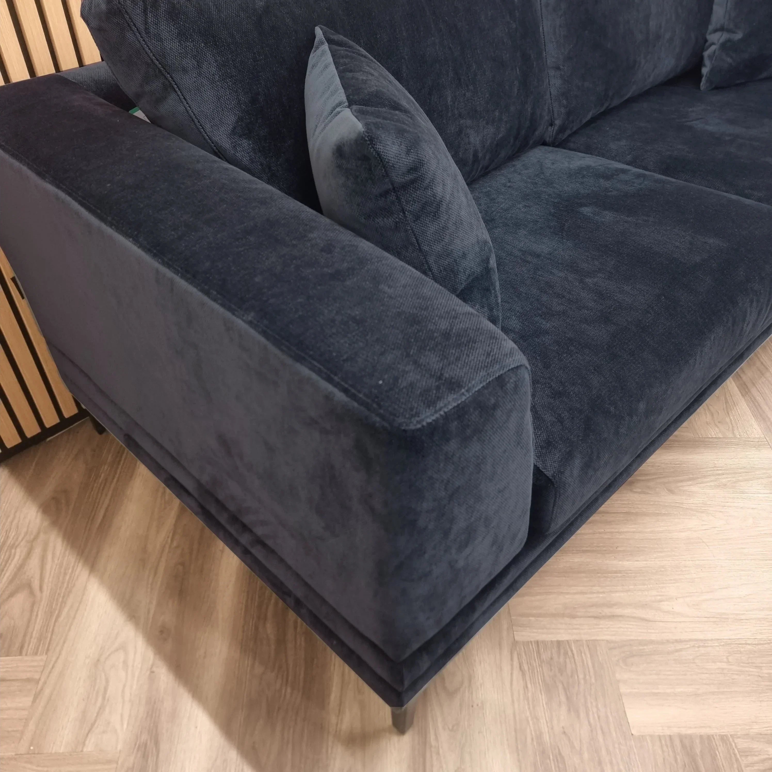 Dark grey fabric sofa with wide armrest and matching cushion on wooden floor