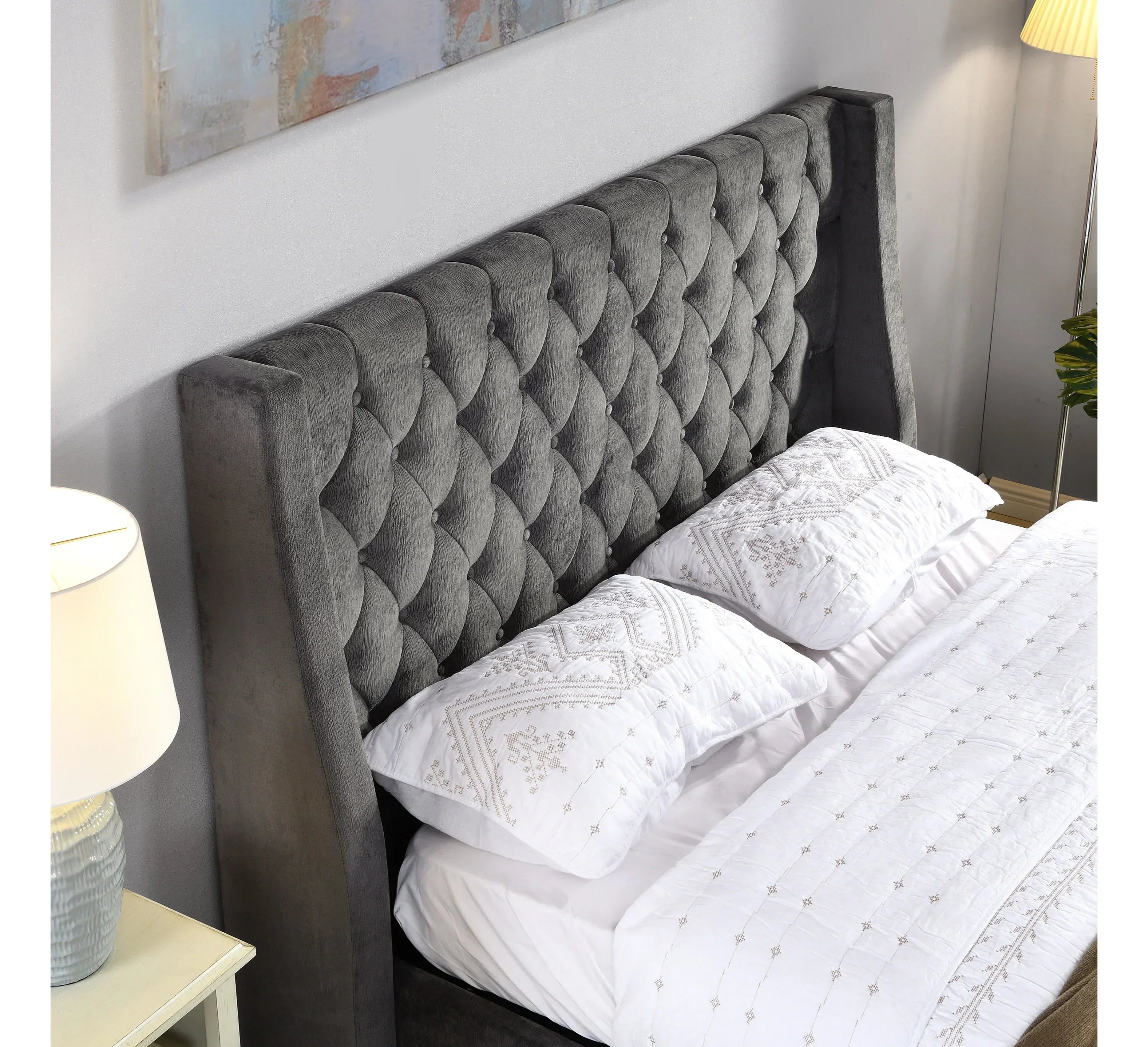 Grey upholstered bed with deep buttoned headboard and white embroidered bedding