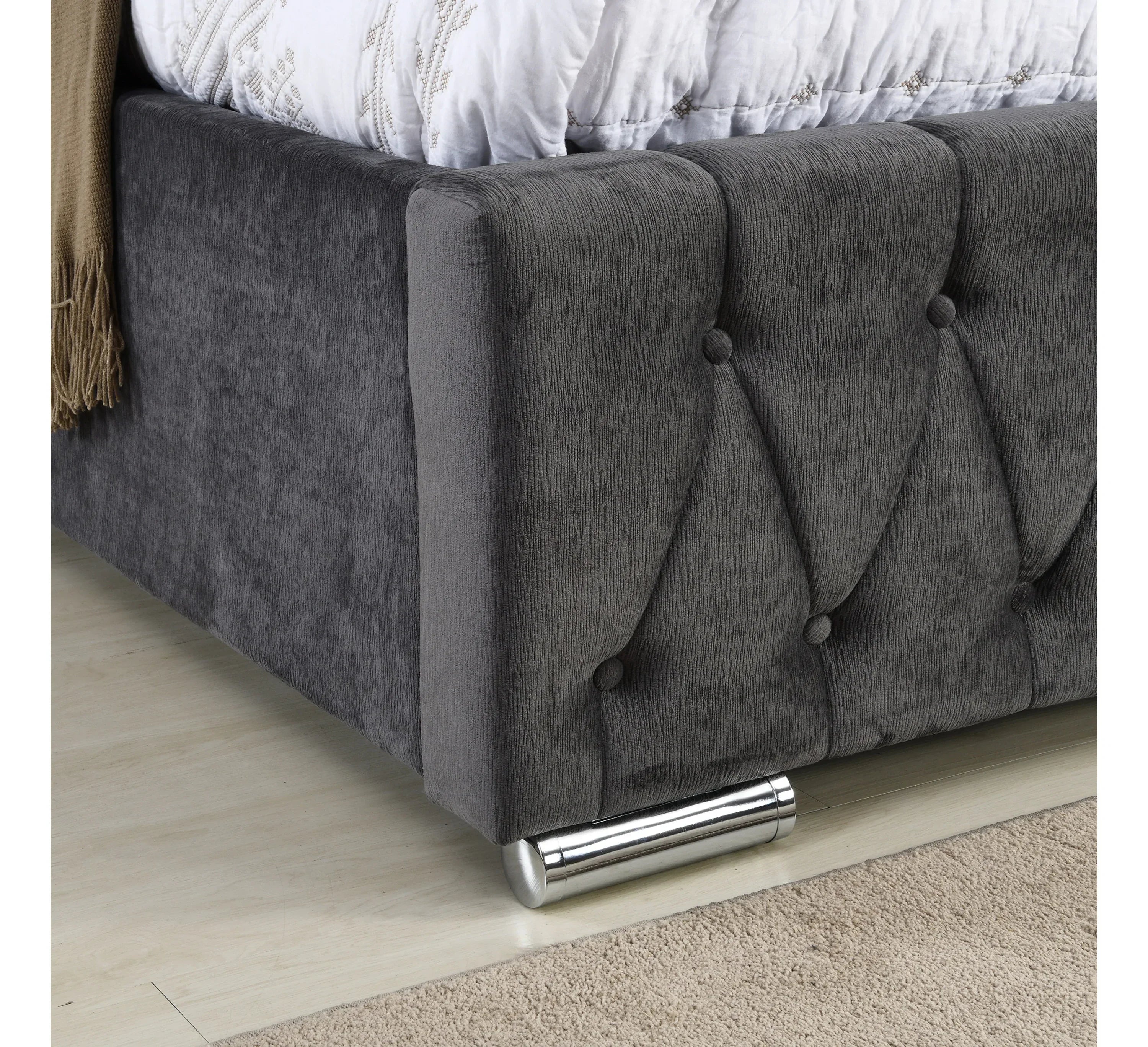Grey upholstered bed frame corner with button tufting and chrome cylinder leg
