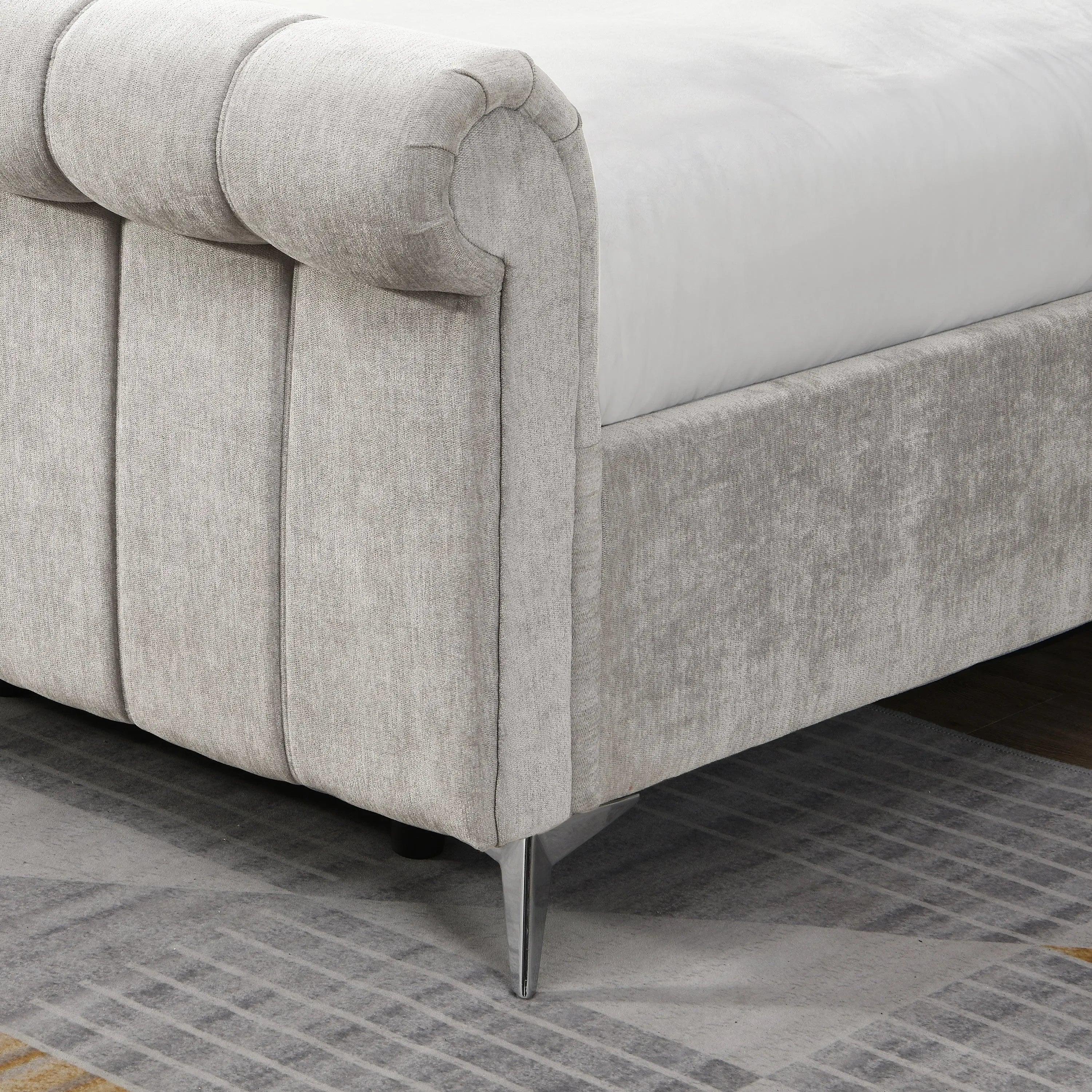 Light grey upholstered bed frame with rolled headboard and chrome legs on patterned rug