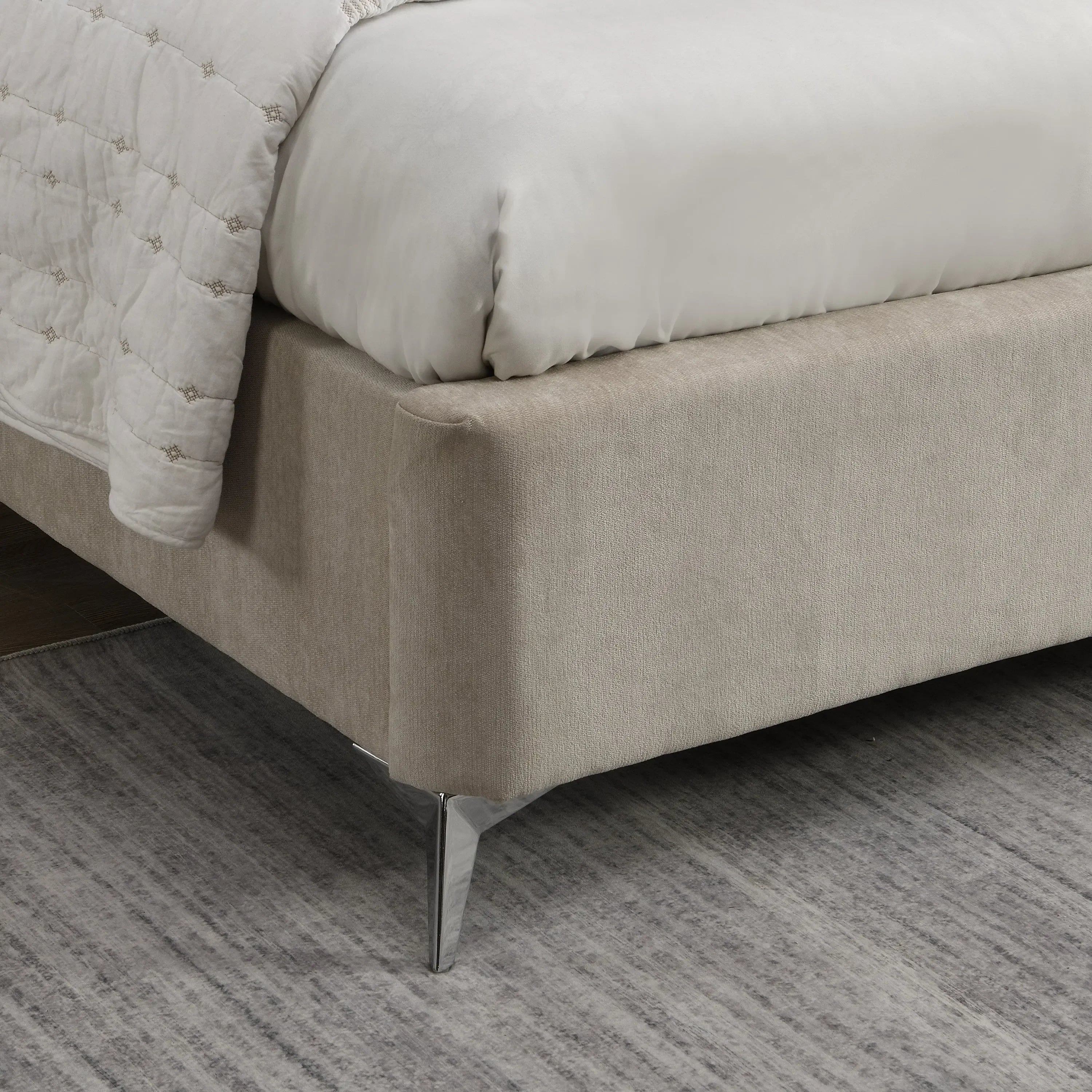 Beige upholstered bed frame corner with metal leg on grey patterned rug