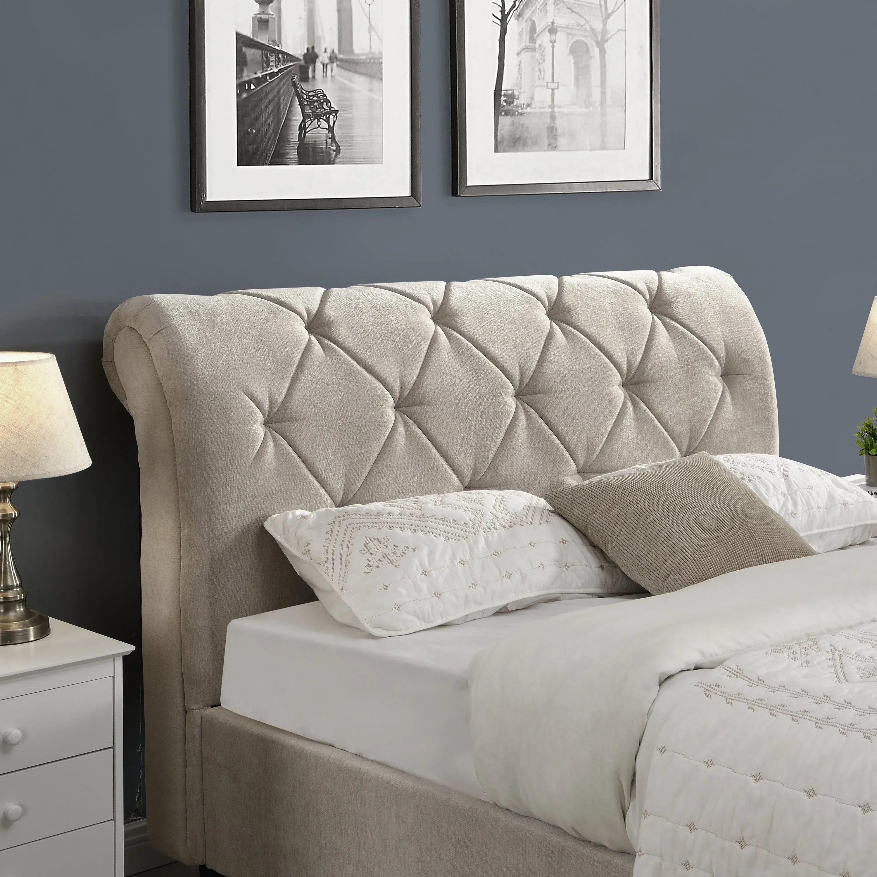 Beige upholstered bed with tufted headboard, white bedding, and bedside table with lamp