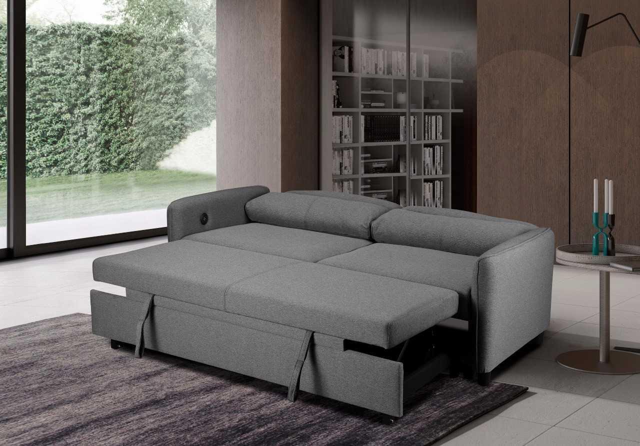 Grey fabric corner sofa bed extended in modern living room with large windows and bookshelf
