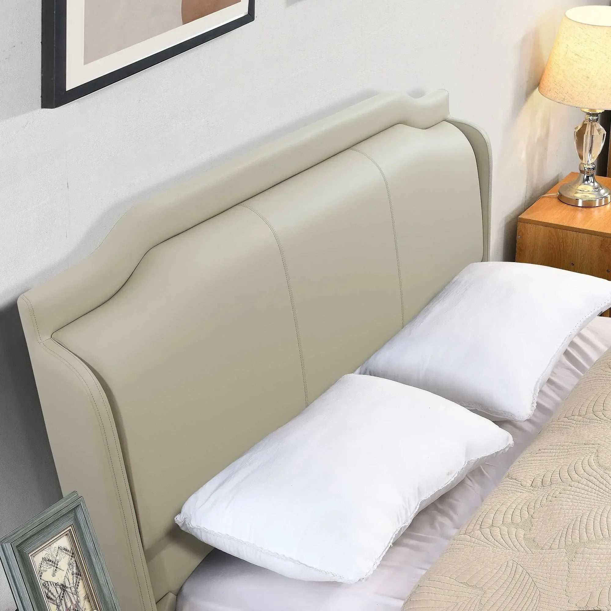 Cream upholstered bed with padded headboard, white pillows and beige quilt, bedside lamp