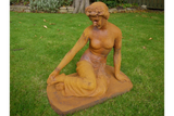 Seated cast iron female garden statue with rust finish on lawn