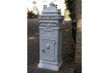 White cast iron post box with ornate detailing on stone driveway by iron gate