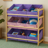 Three-tier kids storage unit featuring a wooden frame with pink and purple fabric bins. The top two tiers have purple bins, while the bottom tier has pink bins. Each bin contains various toys and books, and the unit is placed on a green carpet
