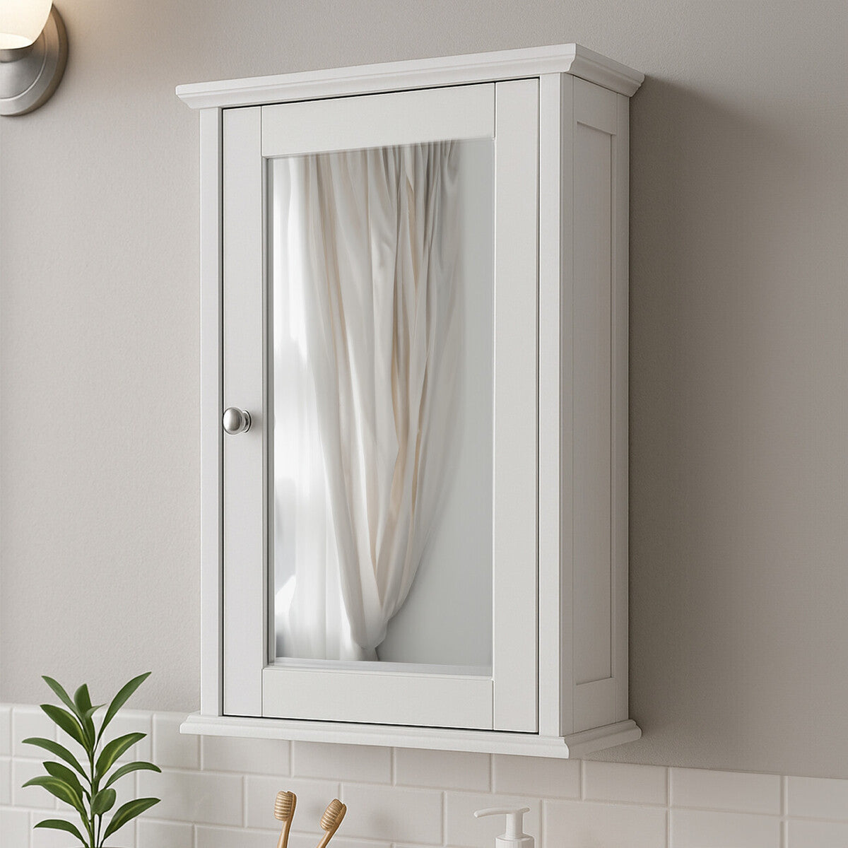 A white mirrored cabinet mounted on a wall, featuring a single door with a mirror front and a small handle. The cabinet has a simple, modern design and is positioned above a countertop with a plant and other decorative items visible below. Soft lighting illuminates the scene, creating a warm ambiance