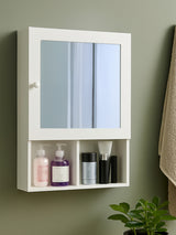 White wood mirrored cabinet with two mirrored doors and an open shelf below, displaying various bottles and containers. The cabinet is mounted on a wall with a neutral-colored background and a towel hanging nearby