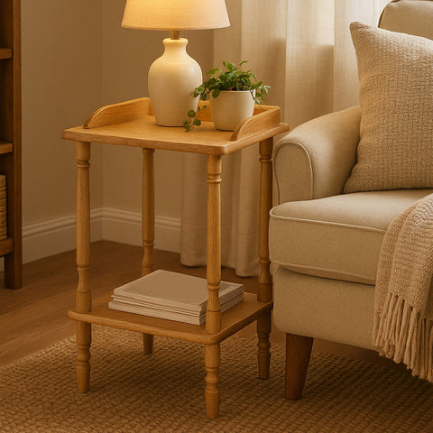 A light-colored Hevea wood side table with a tray-like top, featuring rounded edges and a lower shelf. A small potted plant and a decorative lamp are placed on the table, which stands next to a beige upholstered sofa in a cozy living room setting. Soft natural light filters through sheer curtains, creating a warm atmosphere