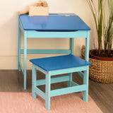A blue children's desk with a slanted top and a matching stool, both featuring a light blue finish. The desk has a small compartment on top, and the stool is positioned beside it on a light-colored rug, with a potted plant visible in the background