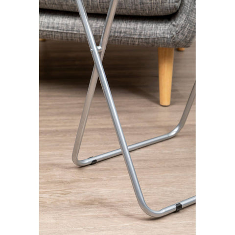 Folding table with a white top and silver metal legs, positioned on a wooden floor, partially visible next to a textured gray sofa