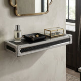 Small wall shelf featuring a crocodile leather effect, mounted against a textured wall. The shelf holds a decorative black tray with small items, a glass box, and a bottle of perfume. A round mirror with a gold frame is visible above the shelf, reflecting light from a nearby window