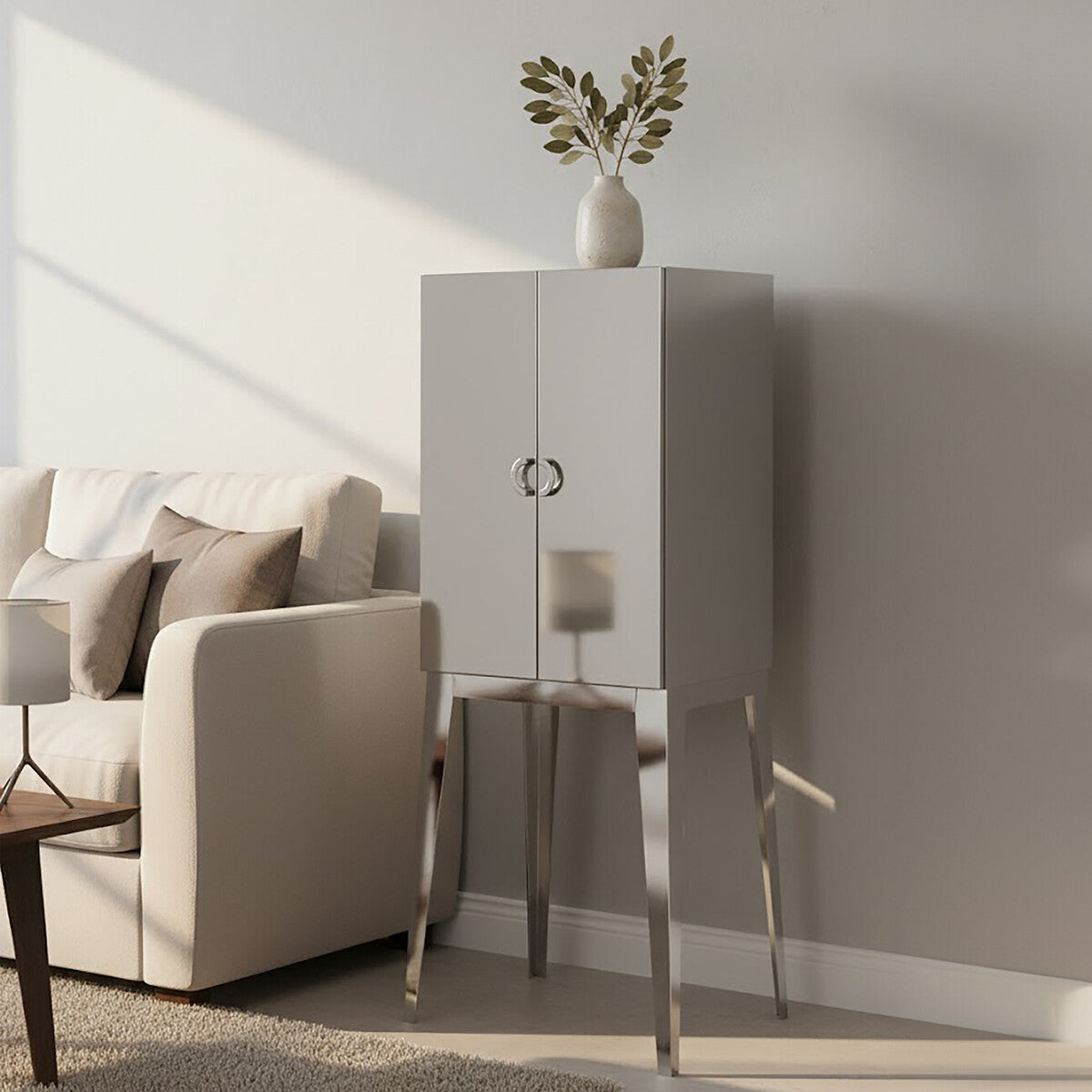 A modern stainless steel two-door cabinet with a sleek white finish, featuring a round handle and standing on slender metallic legs. The cabinet is positioned next to a cozy sofa adorned with light-colored cushions, and a decorative butterfly sculpture is placed on top, adding a touch of elegance to the setting. The background showcases a softly lit room with neutral wall colors
